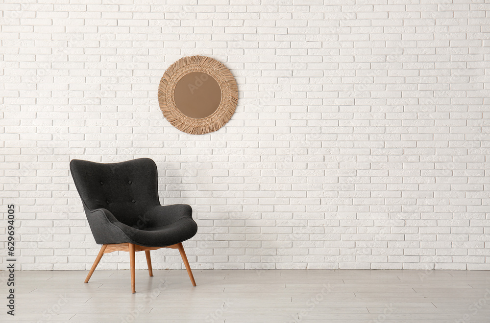 Stylish black armchair and mirror near white brick wall