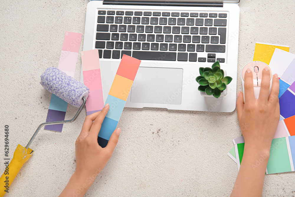 Female hands, color palettes, paint roller and laptop on light background