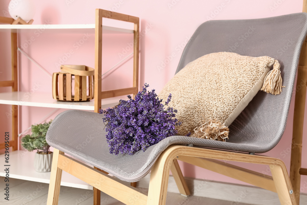 Bouquet of beautiful lavender flowers on chair and shelving unit with decor near pink wall in room, 