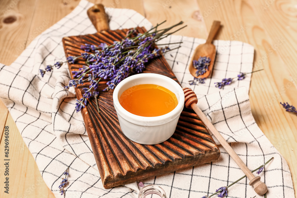 Board with bowl of sweet lavender honey, dipper and flowers on wooden background