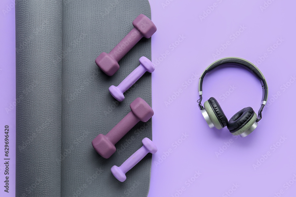 Set of dumbbells, headphones and yoga mat on lilac background