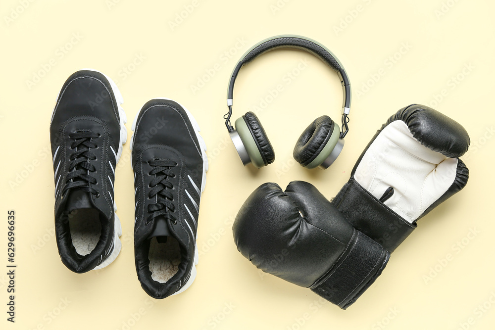 Boxing gloves, sneakers and headphones on color background