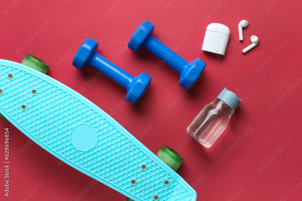 Skateboard, dumbbells, bottle of water and earphones on color background