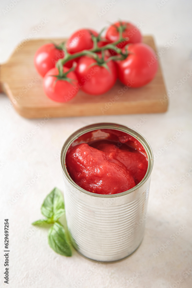 Tin can with tomatoes on light background