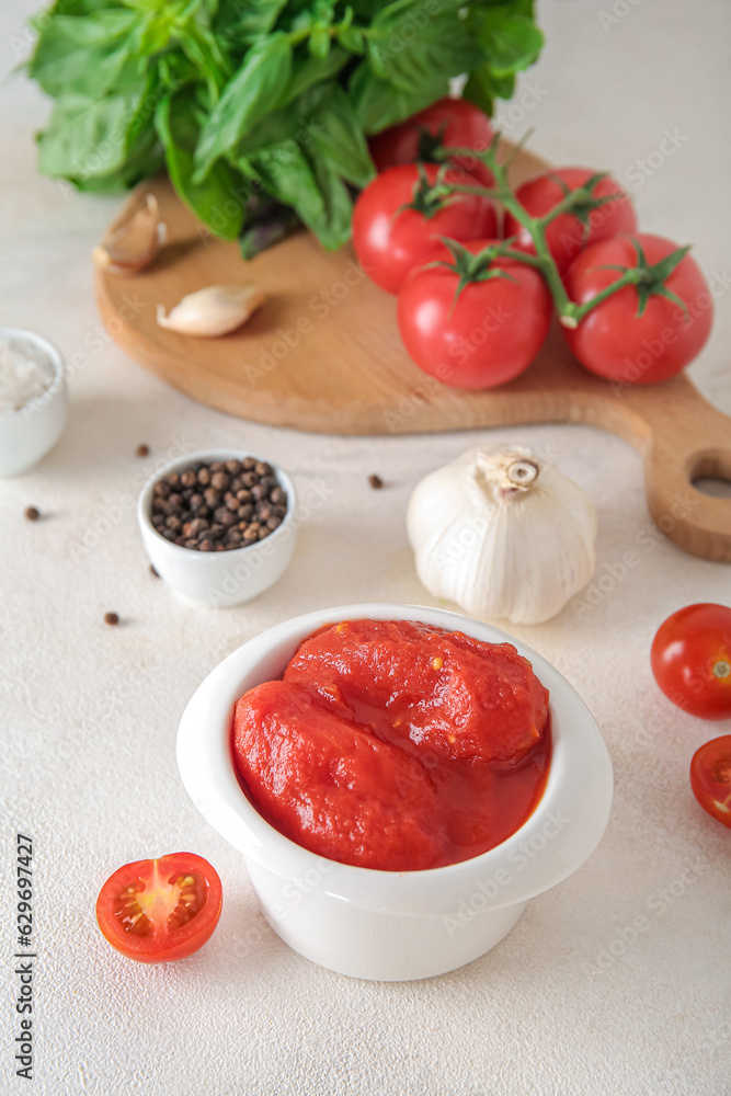 Bowl of canned tomatoes and spices on light background