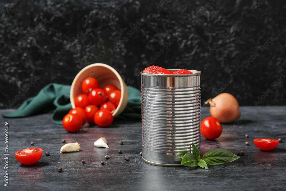 Tin can with tomatoes and spices on dark background