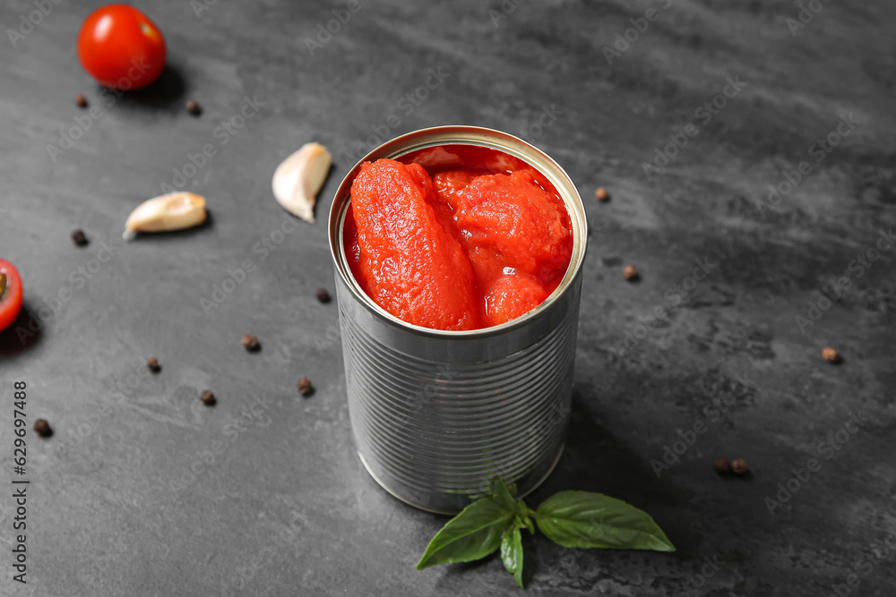 Tin can with tomatoes and spices on dark background