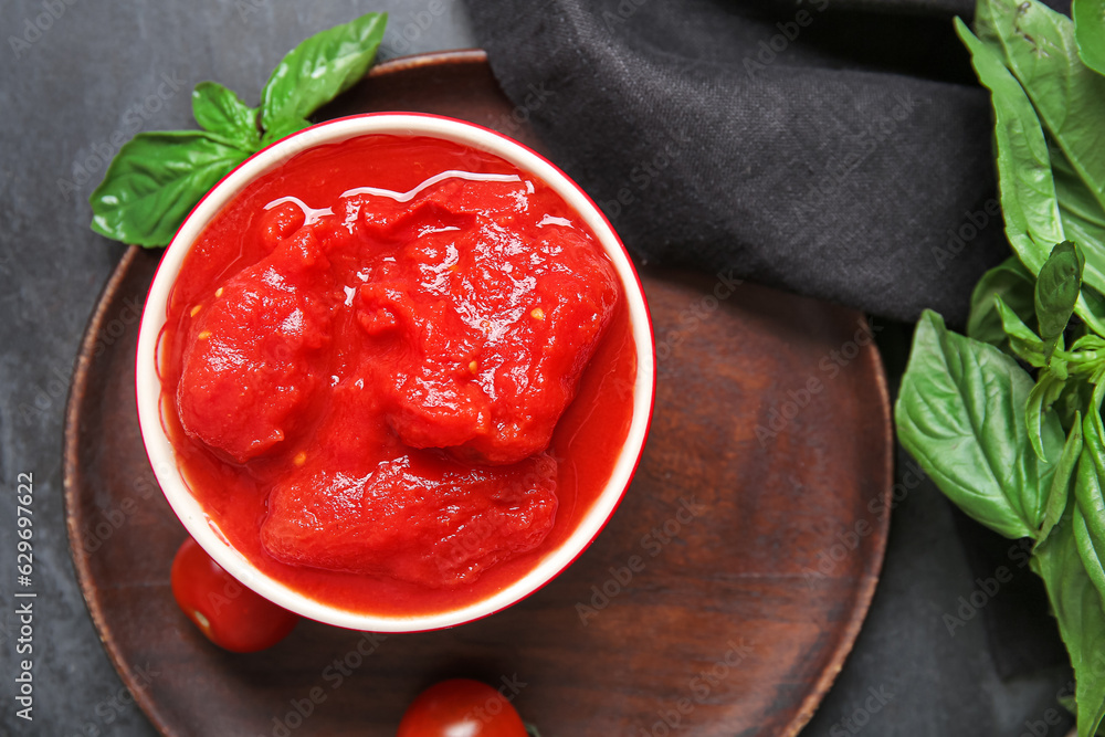 Bowl of canned tomatoes on dark background, closeup