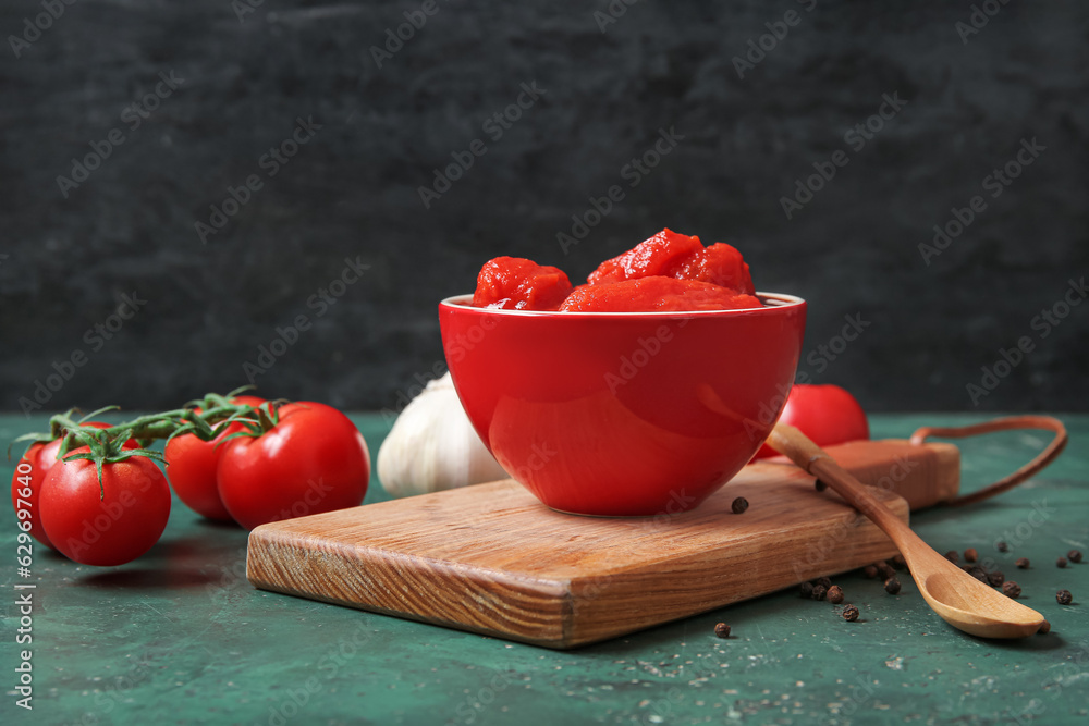 Wooden board with bowl of canned tomatoes and spices on color background