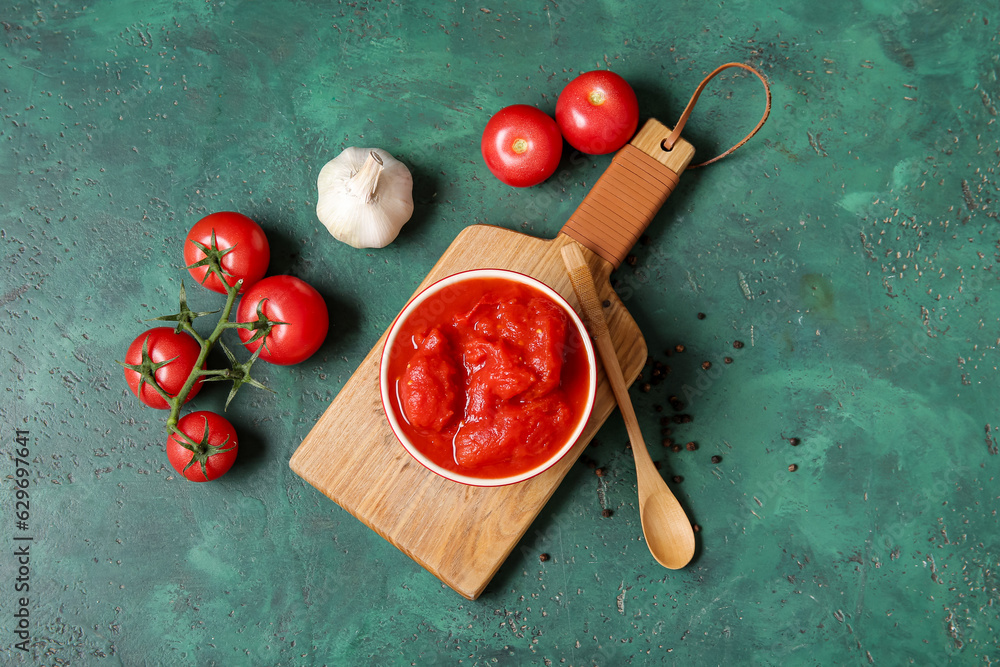 Wooden board with bowl of canned tomatoes and spices on color background