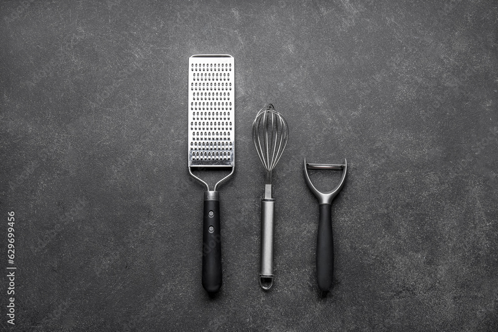 Grater, whisk and vegetable peeler on dark background