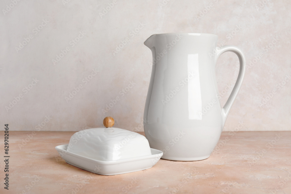 Ceramic butter dish and pitcher on color table against light background