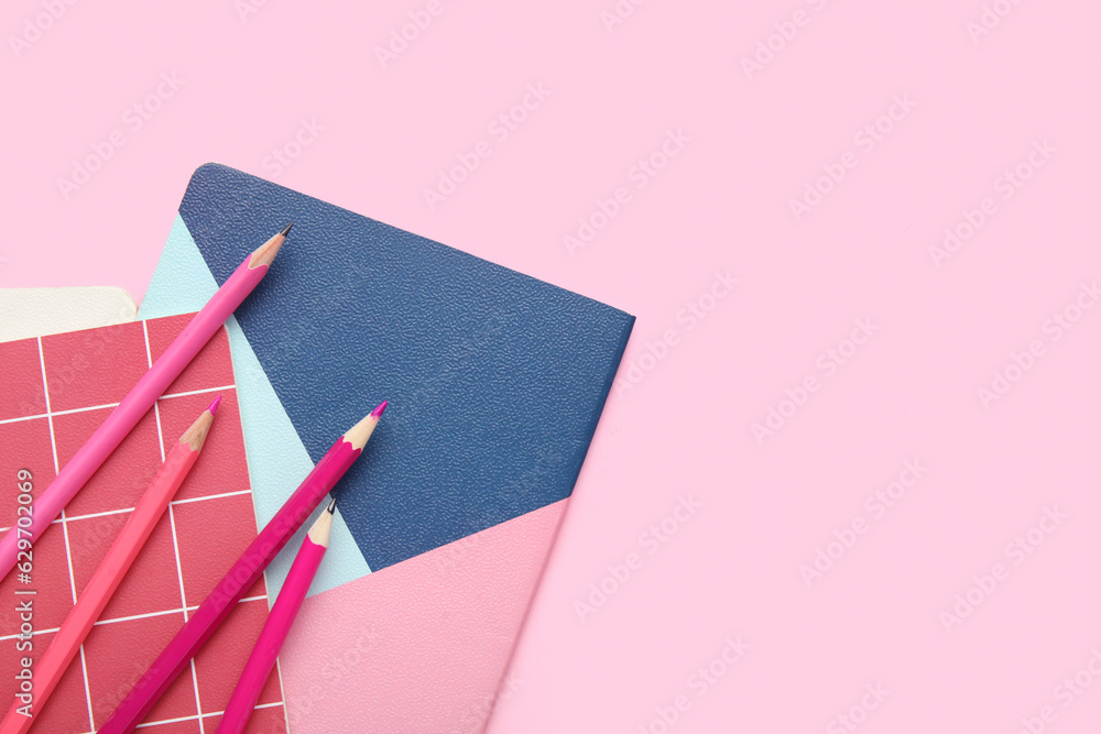 Notebooks and pencils on pink background