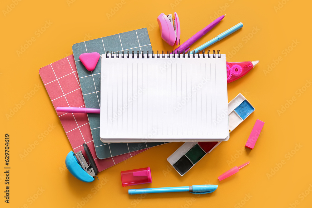 Composition with blank notebook and different school stationery on orange background