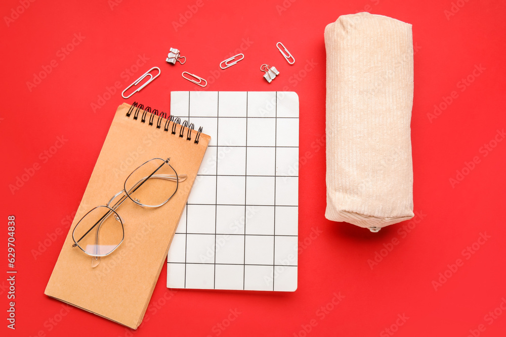 Composition with notebooks, pencil case and eyeglasses on red background