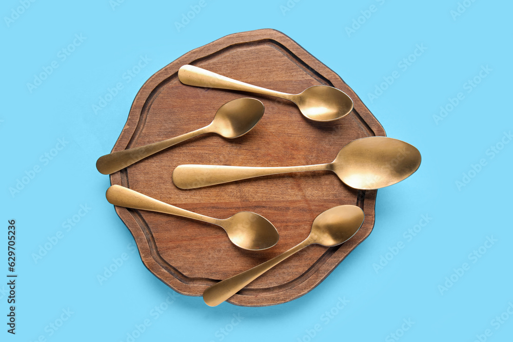 Wooden board with different spoons on color background