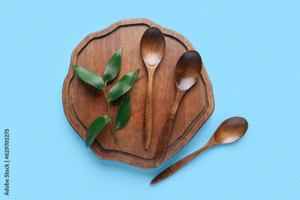 Wooden board with spoons and plant leaf on color background