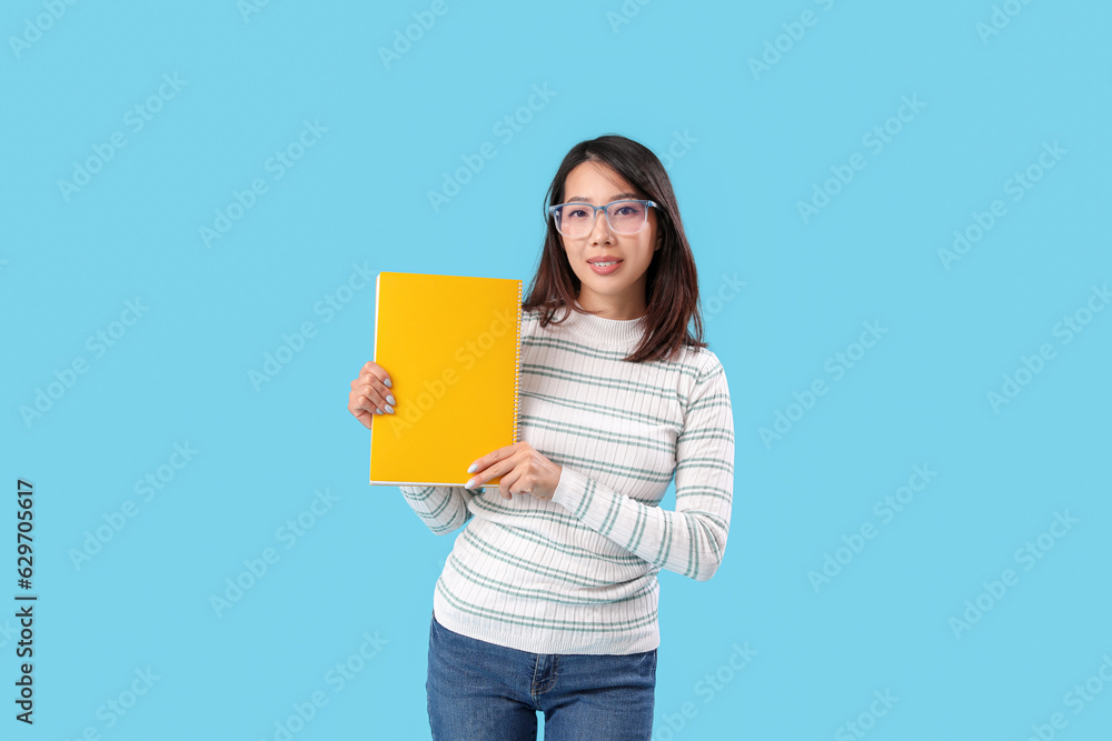 Female Asian teacher with notebook on blue background