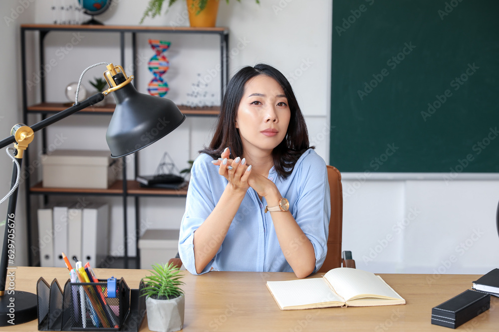 Female Asian teacher sitting at table in classroom