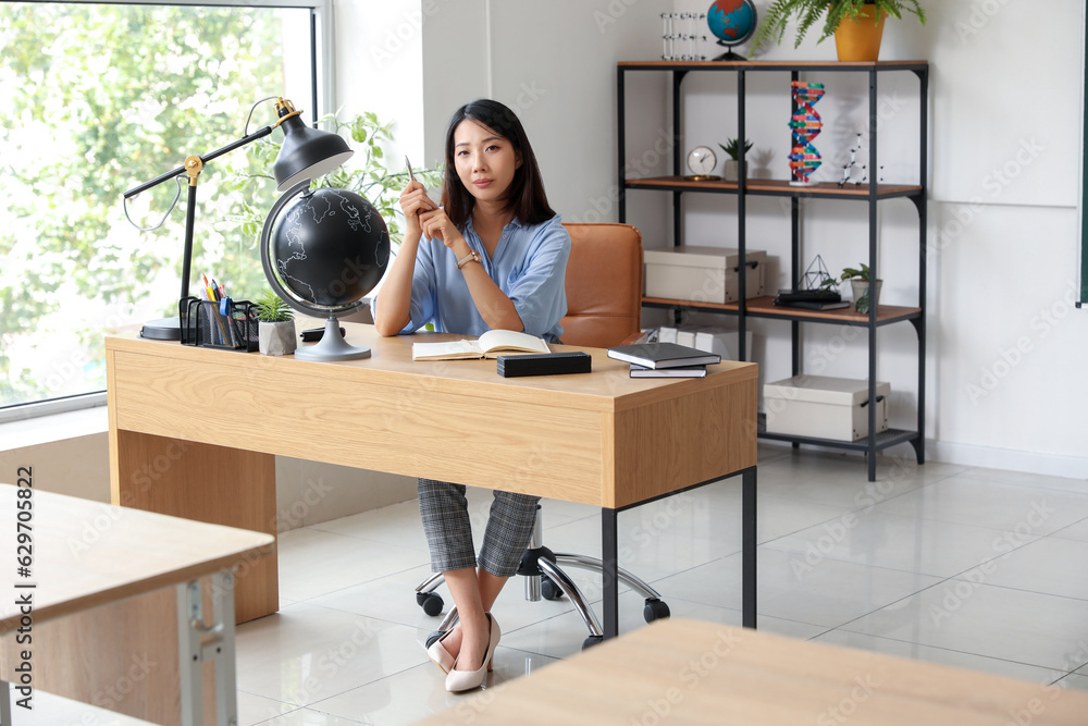 Female Asian teacher sitting at table in classroom