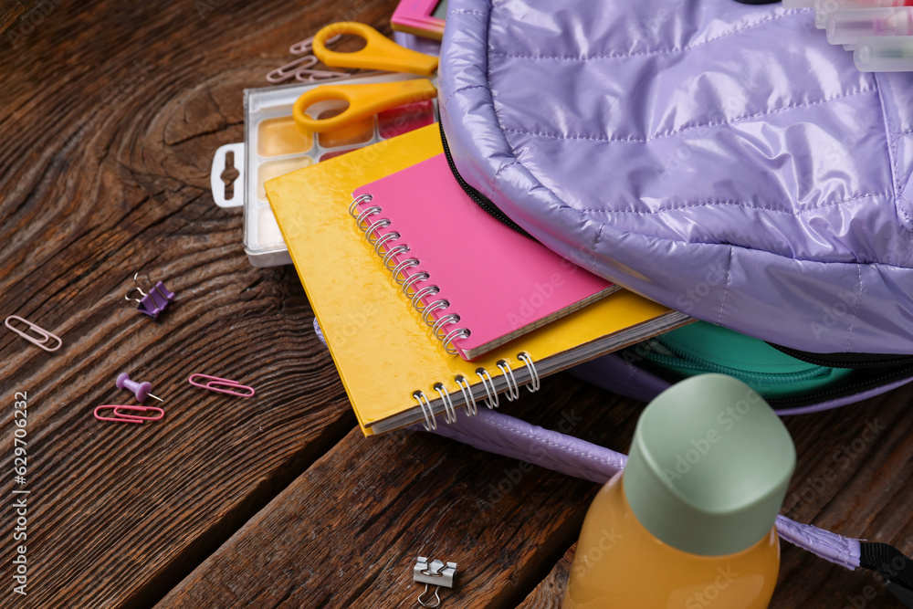 Lilac school backpack with bottle of juice and different stationery on wooden background