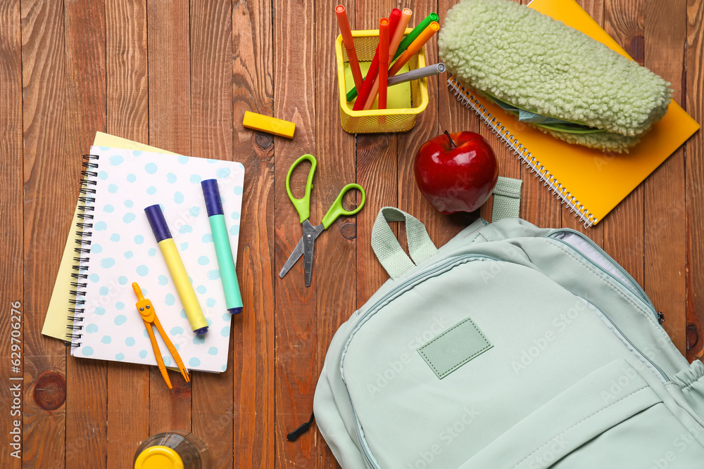 Green school backpack with apple and different stationery on wooden background