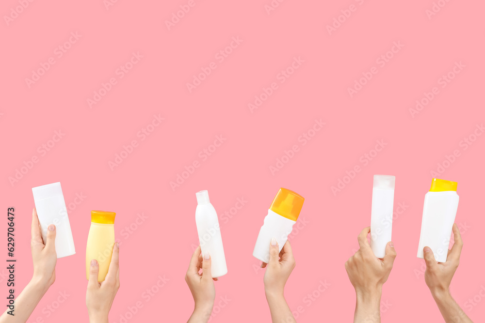 Female hands with bottles of sunscreen cream on pink background