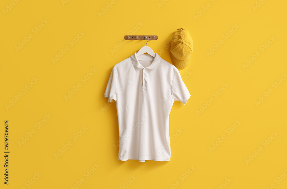 Stylish white t-shirt and cap hanging on yellow background