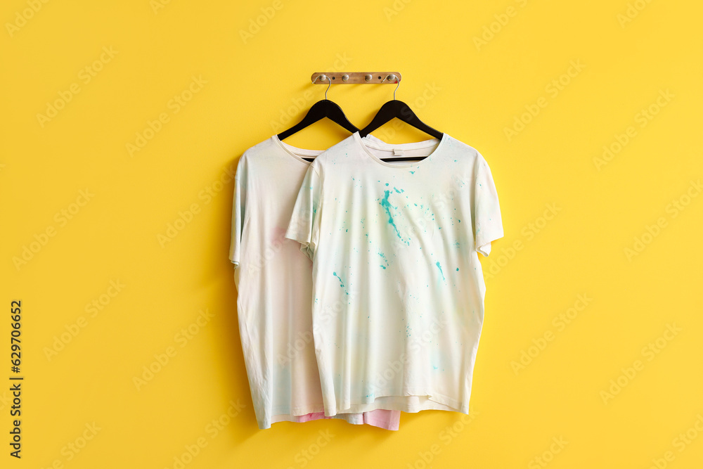 Stylish white t-shirts hanging on yellow background