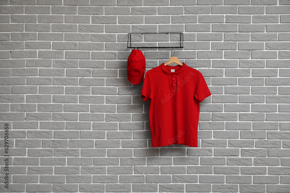 Stylish red t-shirt and cap hanging on grey brick wall