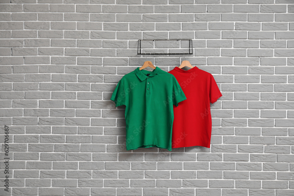 Stylish t-shirts hanging on grey brick wall