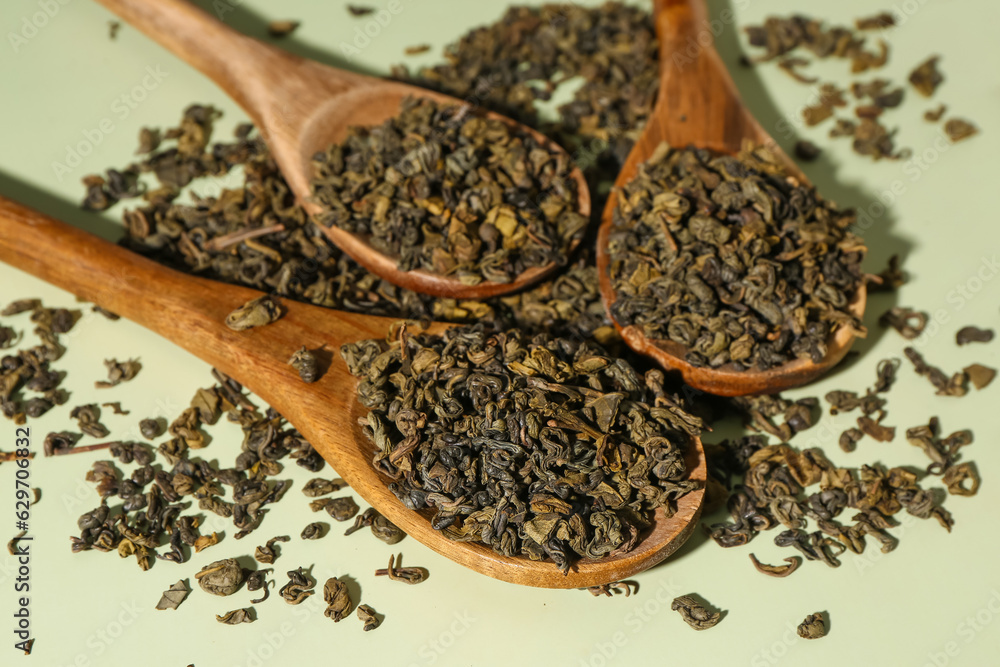 Wooden spoons with dry tea leaves on green background