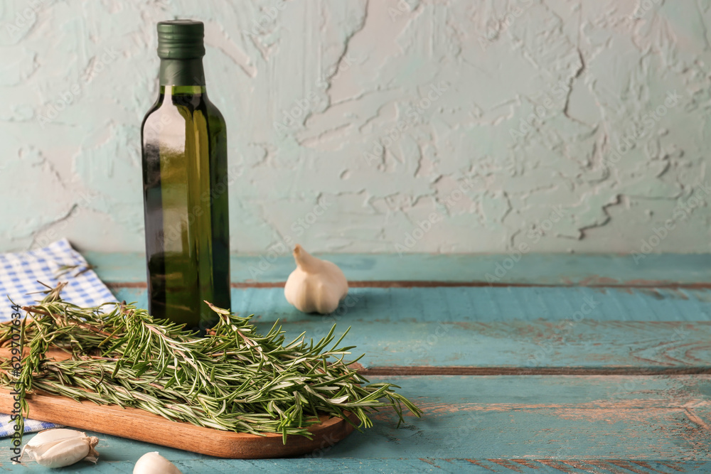 Board with fresh rosemary, garlic and bottle of olive oil on color wooden table