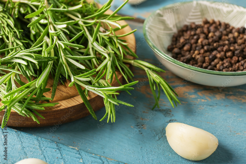 Board with fresh rosemary, garlic and peppercorns on color wooden table, closeup