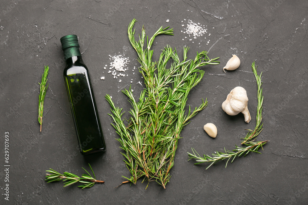 Composition with bottle of olive oil, fresh rosemary and garlic on dark background