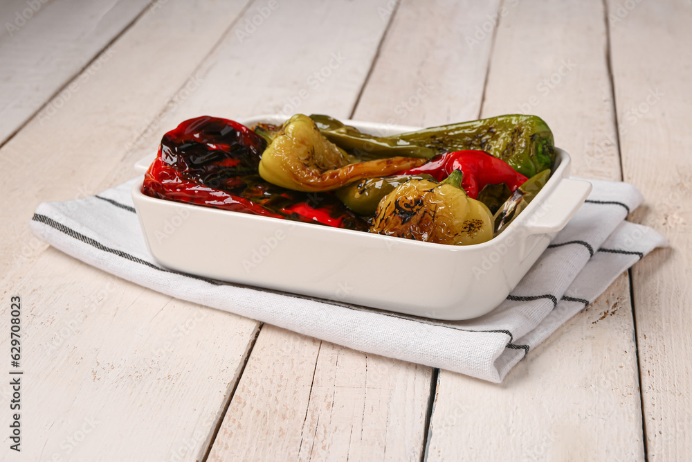 Baking dish with different grilled peppers on light wooden background