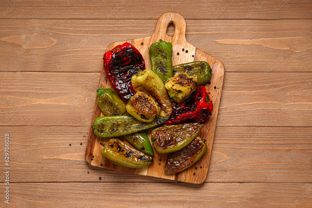 Board with different grilled peppers on wooden background