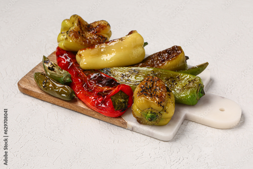 Board with different grilled peppers on grey background