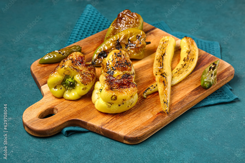 Wooden board with different grilled peppers on blue background