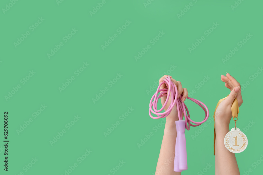 Female hands with jumping rope and medal on green background