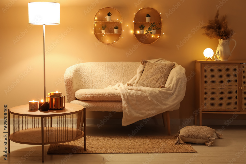 Modern interior of living room with stylish sofa and burning candles on table