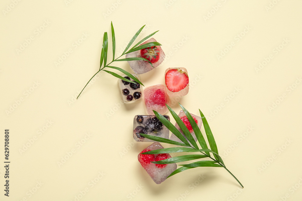 Frozen berries in ice cubes and palm leaves on yellow background