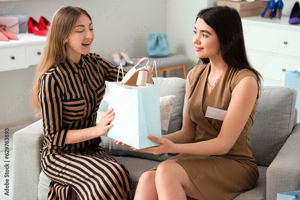 Female sales assistant giving bag with shoes to customer in shop