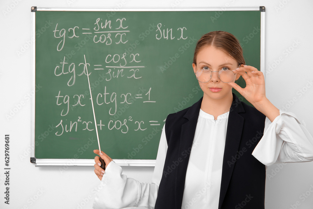 Young math teacher with pointer near blackboard in classroom