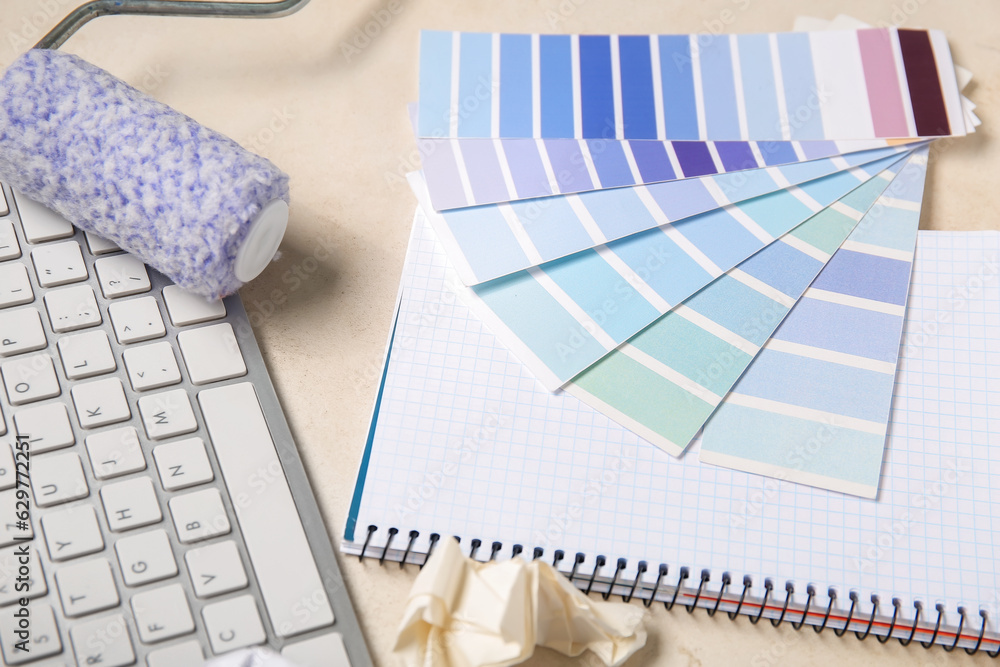 Color palettes, PC keyboard, paint roller and notebook on light background, closeup