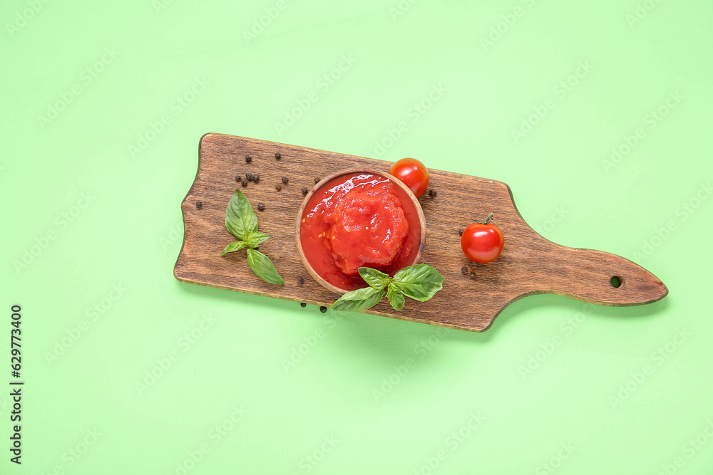 Wooden board with canned tomatoes, peppercorns and basil on green background