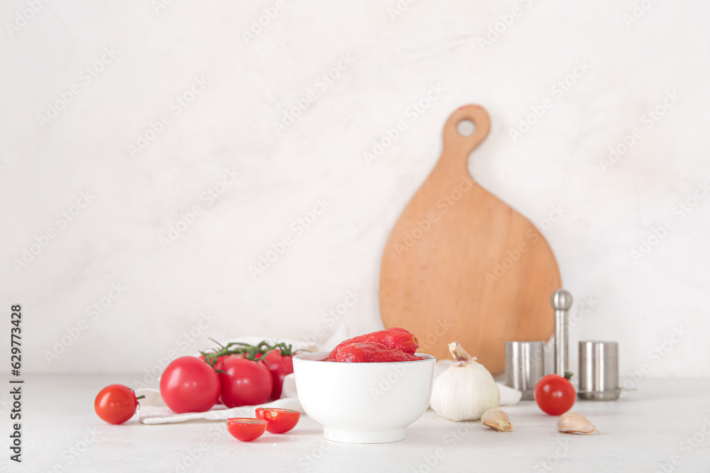 Bowl of canned tomatoes and spices on light background