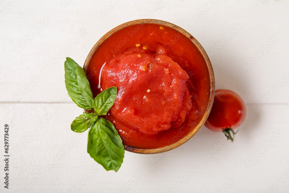 Bowl of canned tomatoes with basil on light wooden background