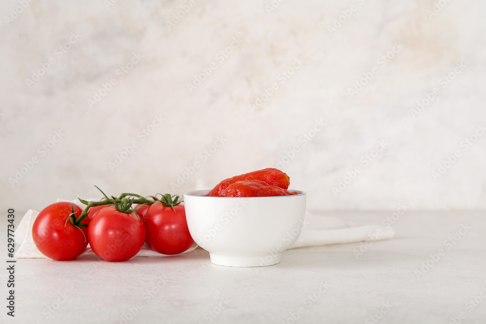 Bowl of canned and fresh tomatoes on light background