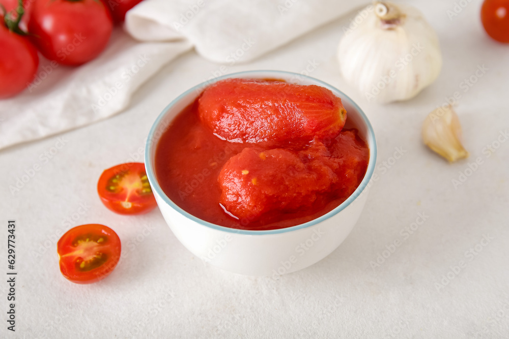 Bowl of canned tomatoes and garlic on light background